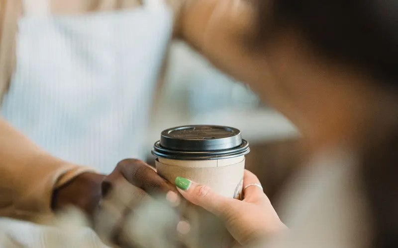A smiling barista passes a takeaway cup across the counter into a customer’s hand.