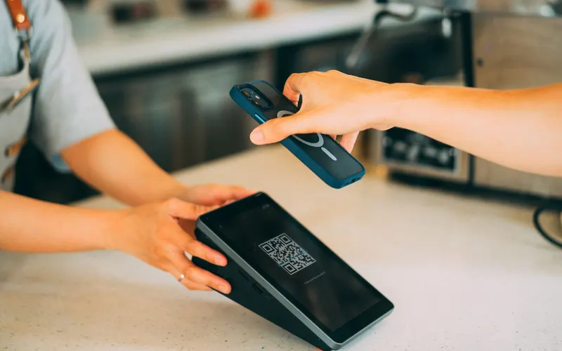 A customer holds their phone out over a café counter towards the shop’s screen, which is showing a QR code.